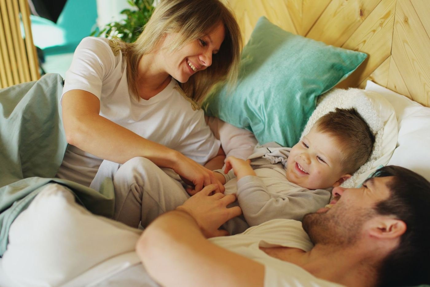 Família reunida na cama pela manhã, com uma criança sorrindo entre os pais